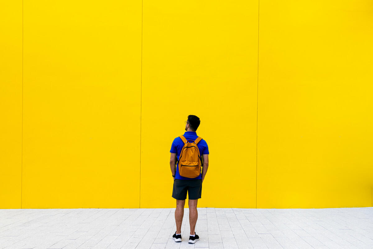 Rückansicht eines Mannes mit Rucksack vor gelber Wand © Alexander Spatari / Getty Images